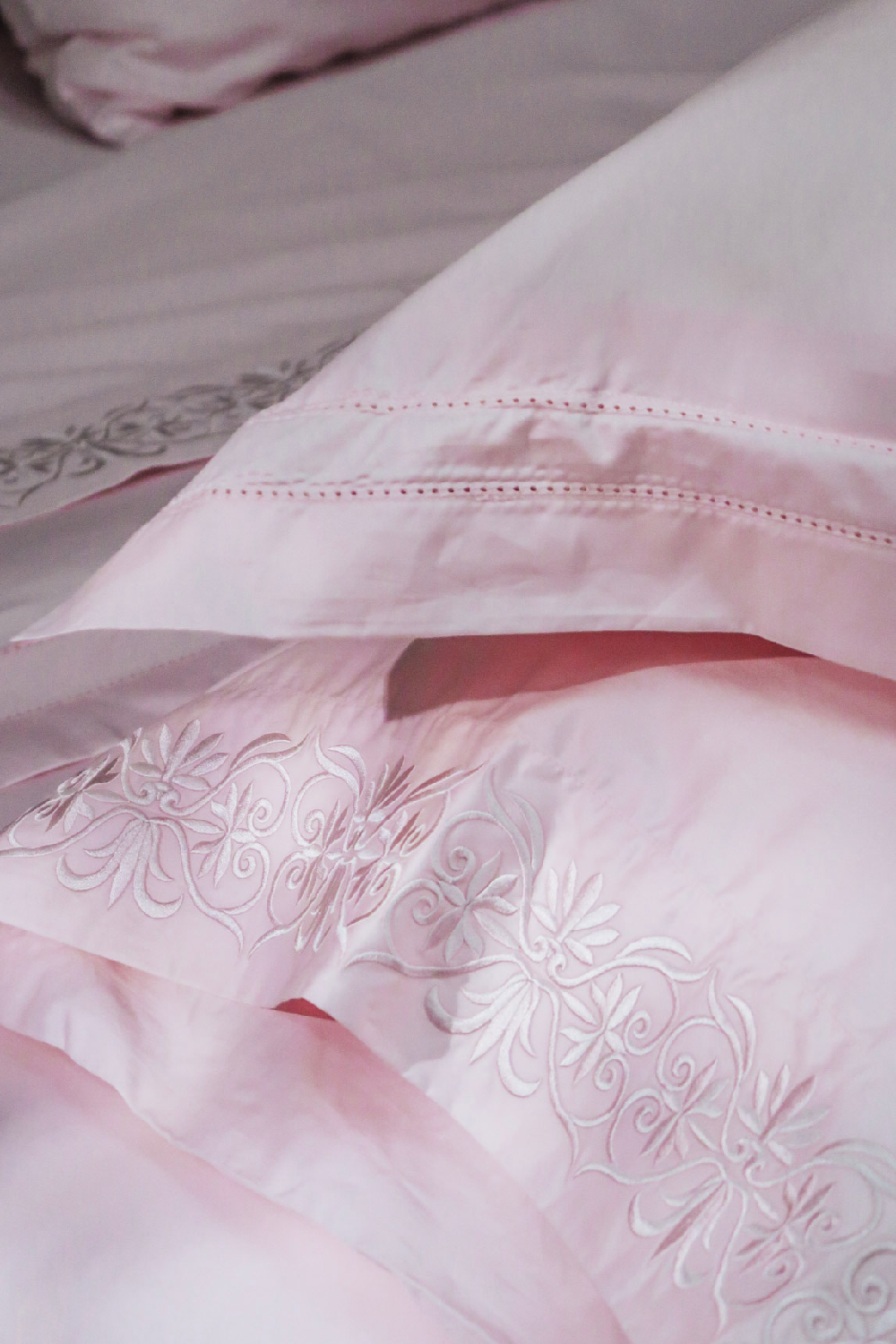 Close-up of a light pink bedding set with embroidered scroll detailing and delicate stitched borders on the pillowcases.
