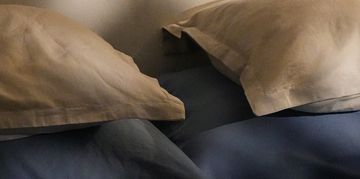 Close-up of two beige pillows resting on dark blue bedding.