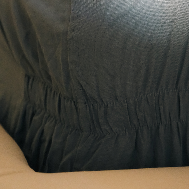 Close-up of a dark charcoal gray fabric garment with a gathered elastic waist, worn by a person whose arm is visible in the foreground.