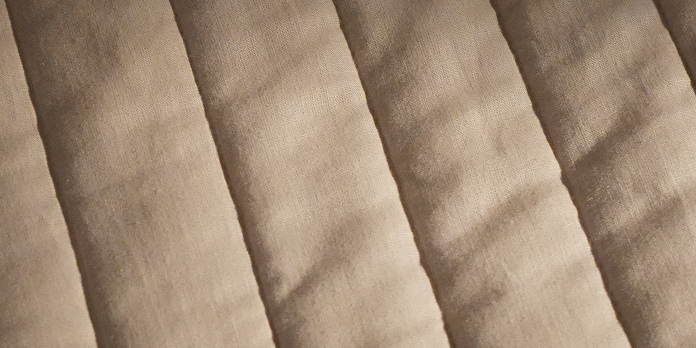A close-up of a beige quilted fabric with stitched vertical channels creating a textured, padded appearance.