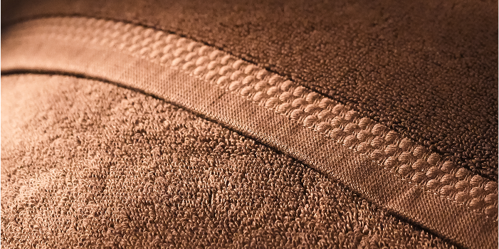 Close-up of a brown textured fabric, likely a bath towel or blanket, with a raised decorative stitched border running diagonally across the frame.