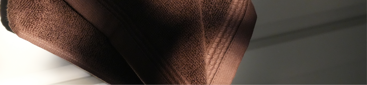 A close-up of a dark brown textured fabric, likely a towel or blanket, draped diagonally with soft light highlighting its woven texture.
