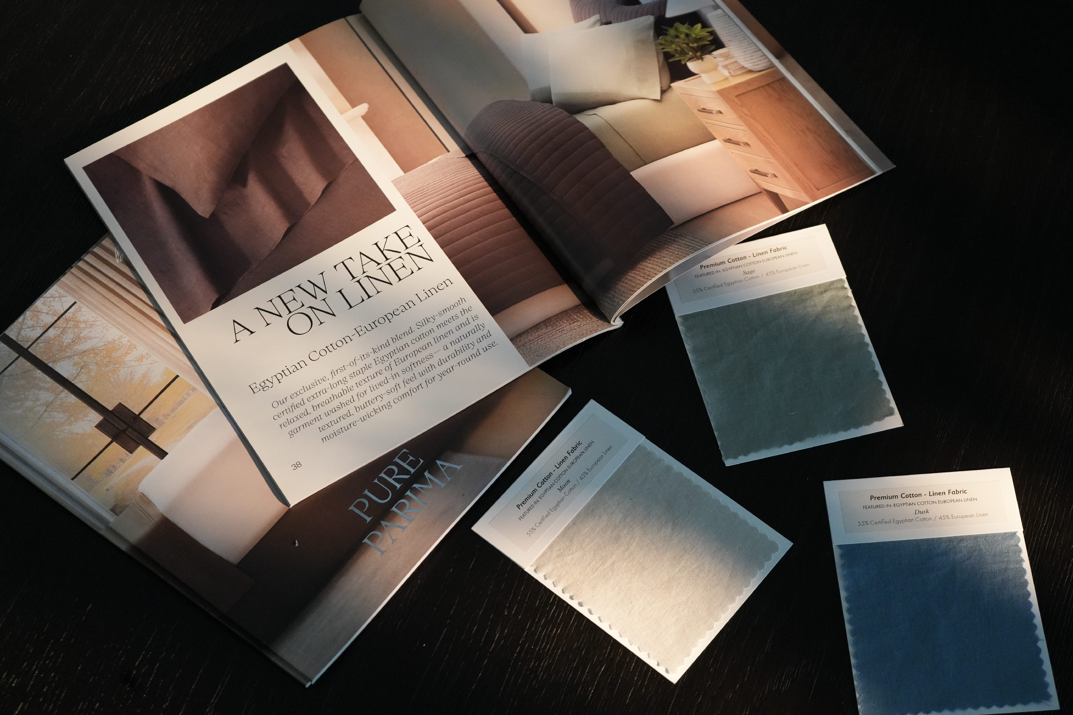 An open interior design magazine or catalog spread on a dark surface, with several small fabric or material swatch cards placed around it. The visible text includes 'A NEW TAKE ON LINEN' and 'PURE PARIMA.