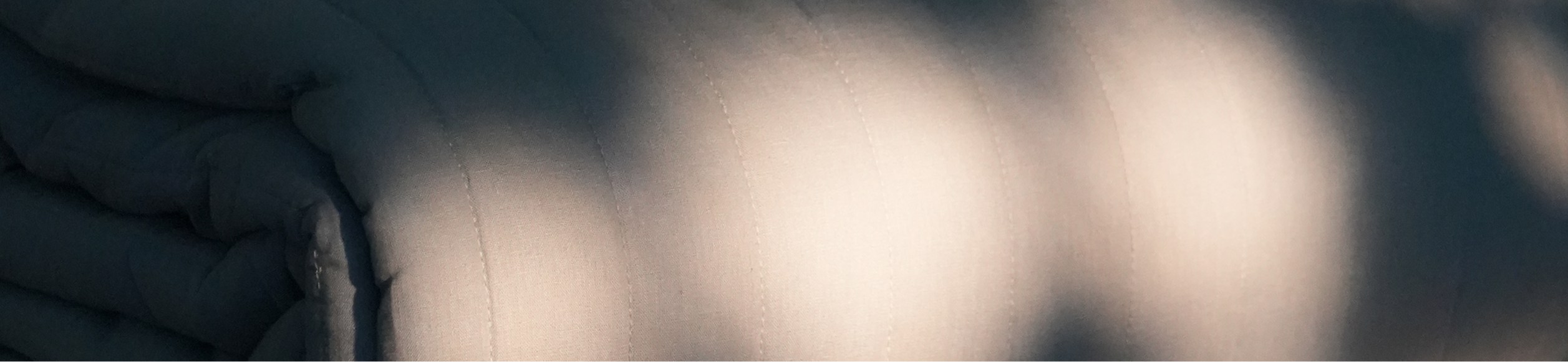 A close-up of a textured gray fabric surface with soft, out-of-focus light patches across it.