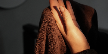 A close-up of a person's hand drying themselves with a dark brown textured towel in warm, low-key lighting.