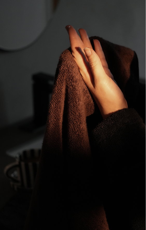 A close-up of a person's hand holding and drying a dark brown towel in dim, warm light.