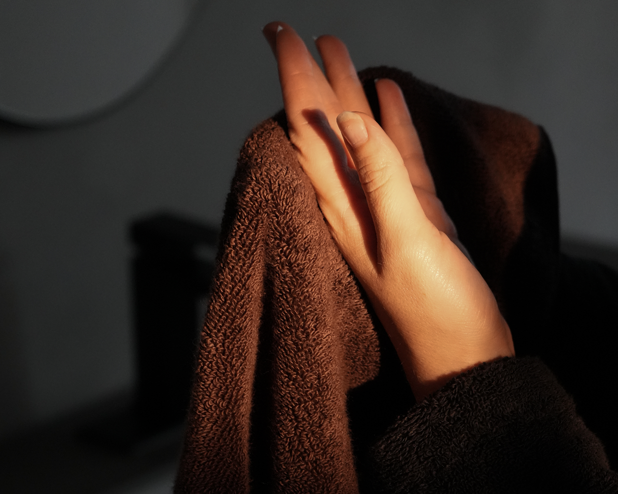 A close-up of a person's hands drying themselves with a dark brown textured towel, captured in dramatic, low-key lighting.