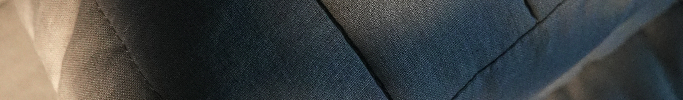A close-up of a dark blue-gray quilted fabric surface with visible stitching and soft texture.
