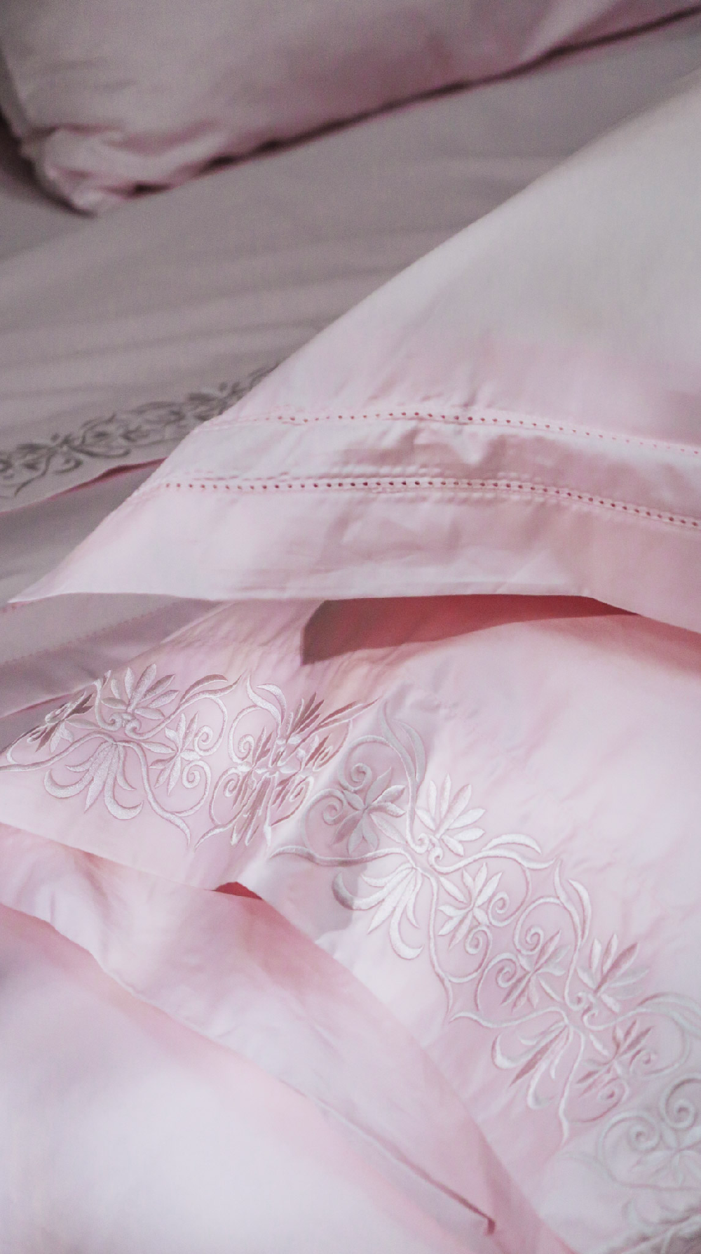 Close-up of a light pink bedding set with embroidered scroll detailing and delicate stitched borders on the pillowcases.