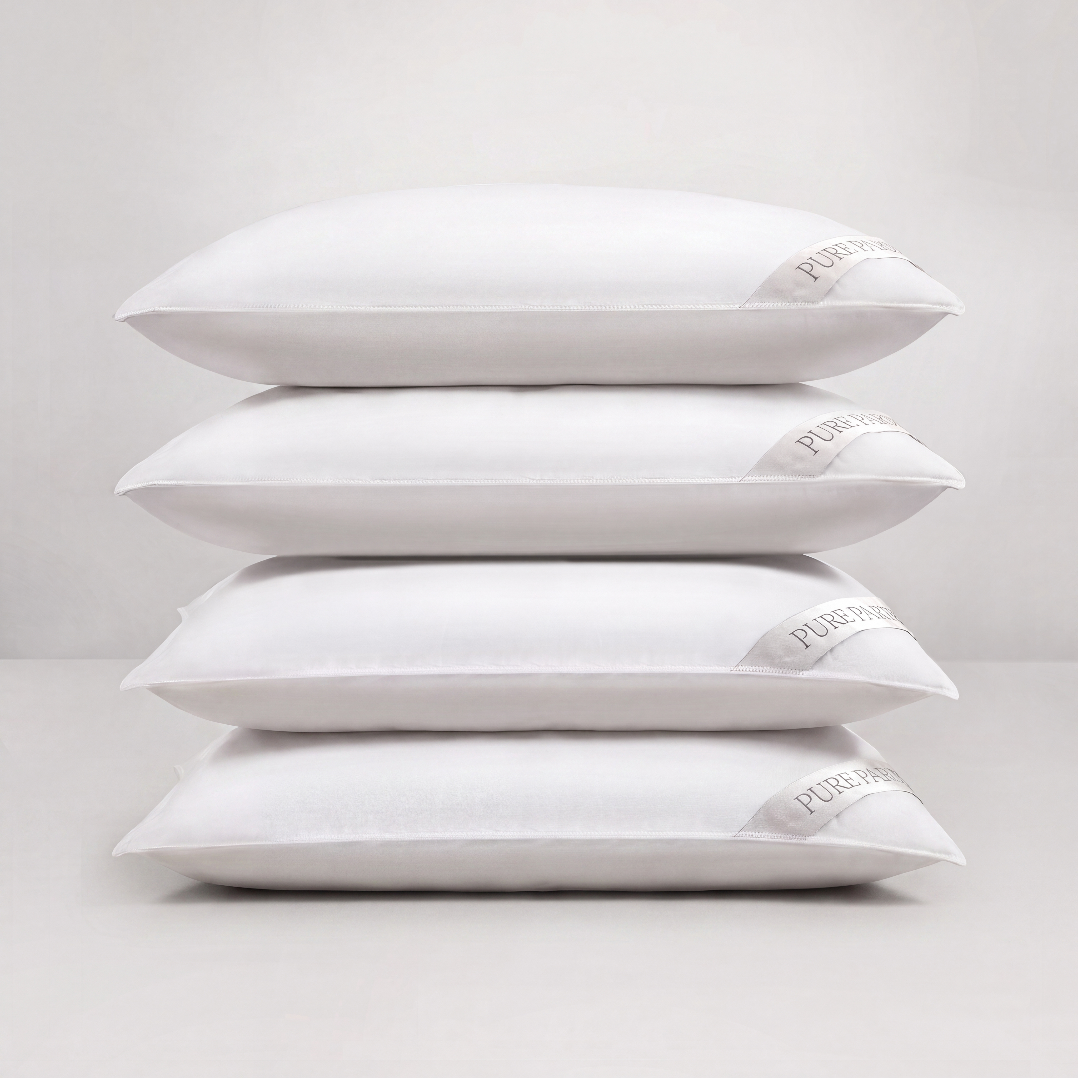 Four white pillows stacked vertically on a light gray studio background. A small fabric tag on the right side of each pillow reads Pure Encapsulated.