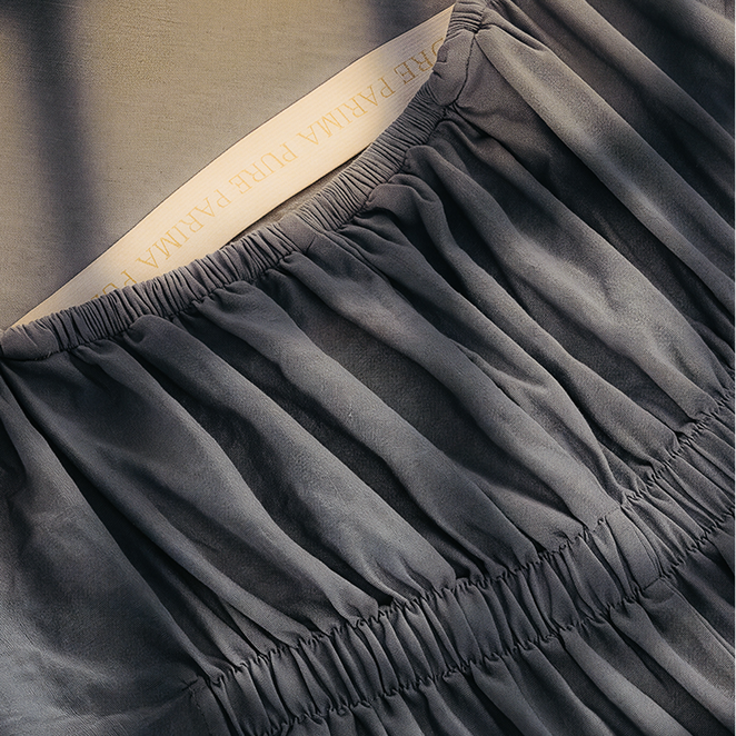 Close-up of a dark gray pleated fabric garment with gathered elastic trim and a cream inner label.