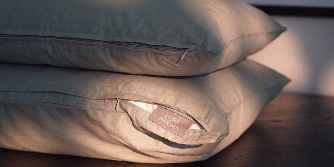 Two stacked pillows in a soft sage green fabric, with a small fabric tag on the lower pillow reading 'PURE PINKA'.