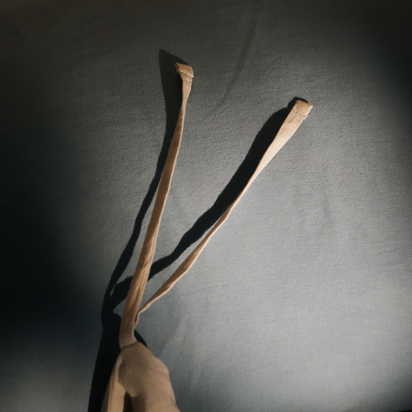 A close-up of a beige fabric strap or tie extending upward against a dark gray background, with strong directional lighting casting a sharp shadow.
